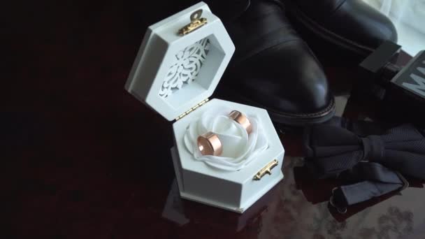 Foto ravvicinata dei dettagli del matrimonio. Una scatola con anelli, scarpe da uomo e papillon. Attributi per un giorno speciale - Filmati, video