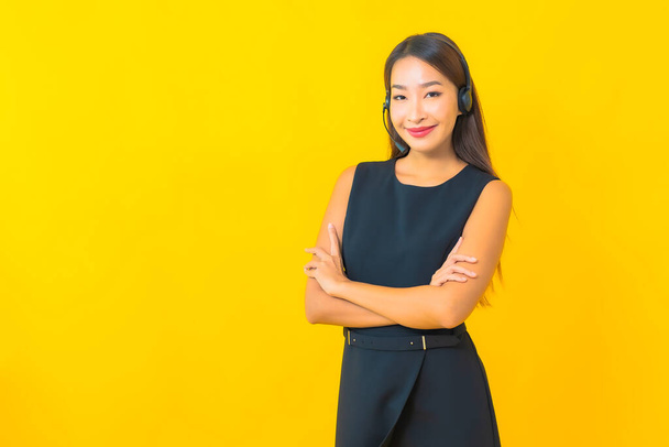 Retrato bonito jovem asiático mulher de negócios com fone de ouvido call center atendimento ao cliente no fundo amarelo - Foto, Imagem