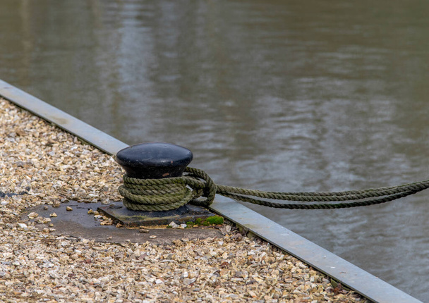 Rope tied to a black mooring bollard on the dock with water in the background. - Photo, Image