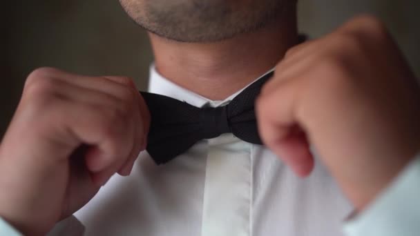 Dichtbij een man die een strikje omdoet. Jonge volwassene in wit shirt met een elegante strik. De bruidegom maakt zich klaar voor de bruiloft. - Video