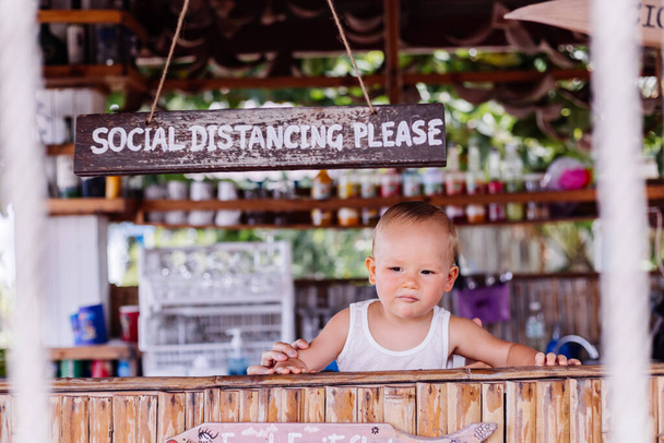 Маленький мальчик в отпуске в Таиланде с табличкой социальной дистанции в баре. - Фото, изображение