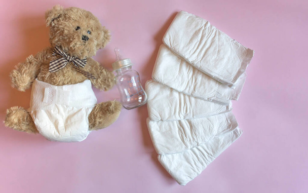 Witte wegwerp luiers voor kleine baby 's op roze achtergrond en schattige teddybeer. Bovenaanzicht, selectieve focus - Foto, afbeelding