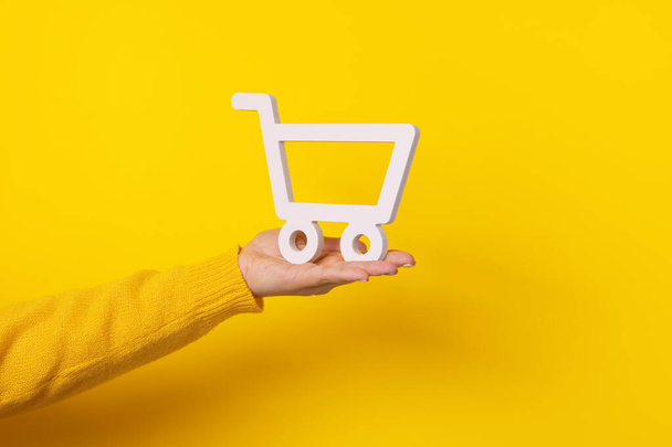 carrito de compras en la mano sobre fondo amarillo - Foto, Imagen