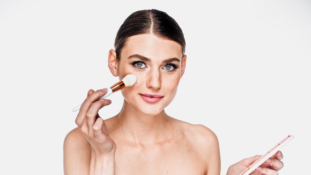 Giovane donna adulta che applica polvere viso sulle guance con pennello cosmetico isolato su bianco - Foto, immagini