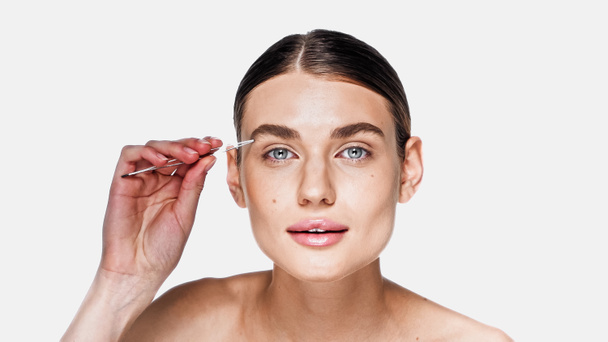 junge Frau mit sauberem Gesicht Styling Augenbraue mit Pinzette isoliert auf weiß - Foto, Bild