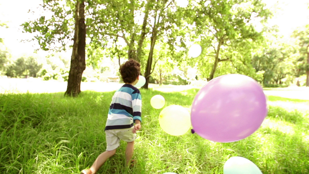 Boy playing with colorful balloons in park - Πλάνα, βίντεο