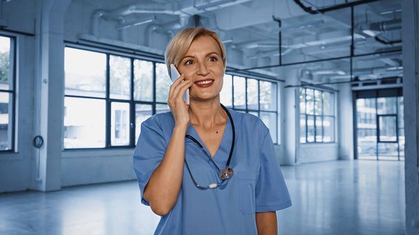 Smiling mature doctor talking on mobile phone in clinic  - Fotografie, Obrázek