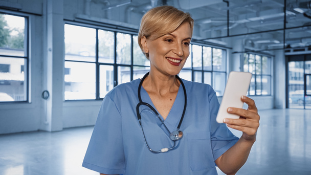 Sorridente medico maturo utilizzando smartphone in ospedale  - Foto, immagini