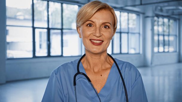 Cheerful doctor with stethoscope looking at camera in clinic  - Foto, Bild