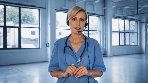 Starší lékař ve sluchátkách a uniforma mluvení před kamerou během konzultace  - Fotografie, Obrázek