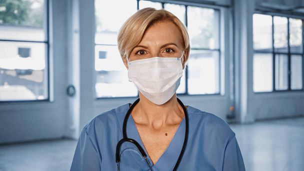 Reifen Arzt in medizinische Maske Blick auf Kamera im Krankenhaus  - Foto, Bild