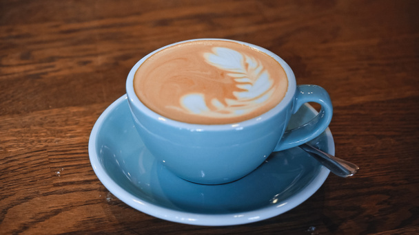 xícara azul de cappuccino delicioso com arte latte na mesa - Foto, Imagem