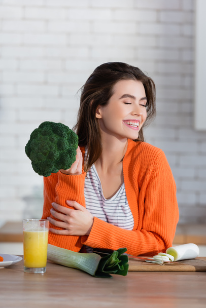 щаслива жінка з закритими очима тримає брокколі біля свіжих овочів на кухні
 - Фото, зображення