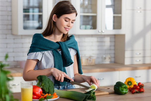 junge lächelnde Frau bereitet in der Küche Frühstück aus frischem Gemüse zu - Foto, Bild