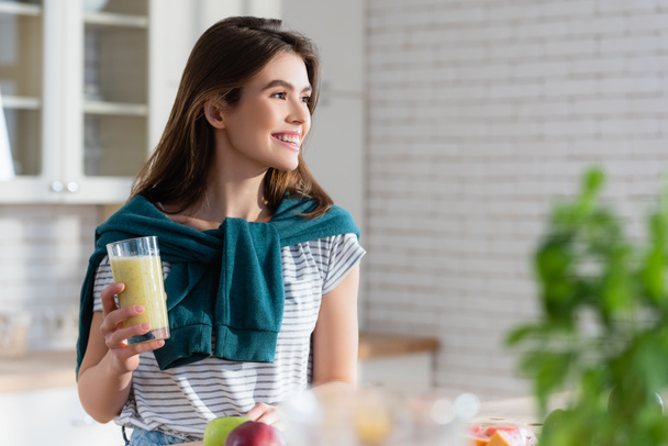 happy woman holding glass of fresh juice on blurred foreground in kitchen - 写真・画像