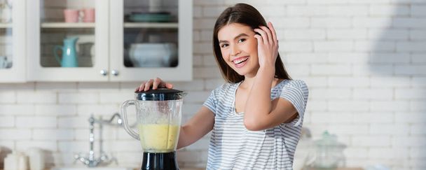happy woman fixing hair while preparing smoothie in blender, banner - Photo, Image