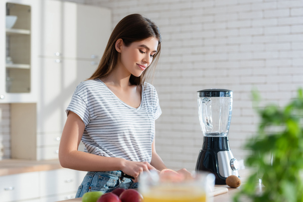 smiling woman preparing breakfast near fresh fruits and blender in kitchen - Photo, Image