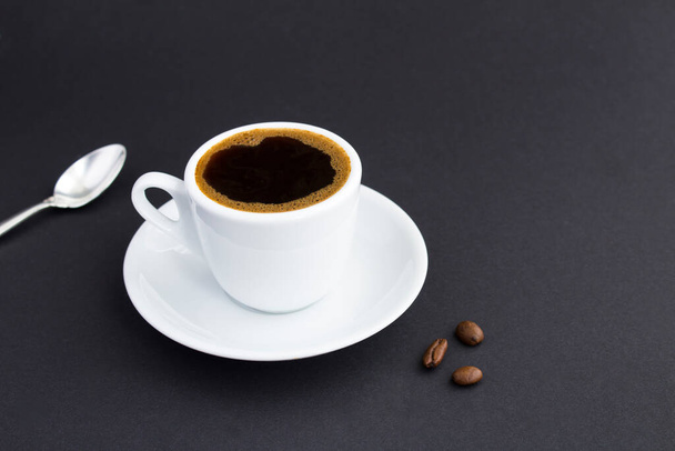Zbliżenie na biały kubek z czarnej kawy i ziaren kawy na ciemnym tle - Zdjęcie, obraz
