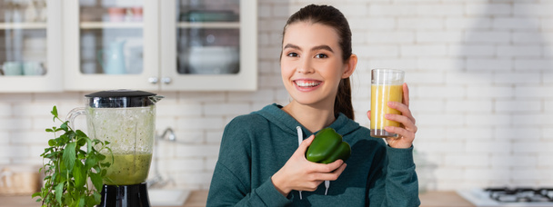 happy woman holding glass of fresh smoothie and bell pepper near blender, banner - Fotoğraf, Görsel