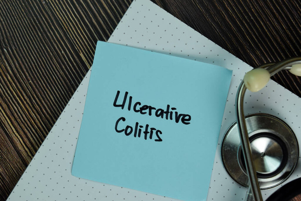 Colitis ulcerosa schreibt auf klebrige Zettel, die isoliert auf dem Holztisch liegen. medizinisches oder medizinisches Konzept - Foto, Bild