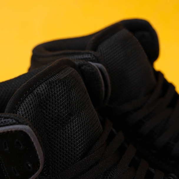 Κοντινό πλάνο ζευγάρι μαύρα sneakers που απομονώνονται σε κίτρινο φόντο. Μαύρη ταπετσαρία παπουτσιών. Mock Up μαύρο sneakers σε κίτρινο φόντο. Κατάλληλο για το διαφημιστικό υλικό σας. Κλείσιμο των sneakers - Φωτογραφία, εικόνα