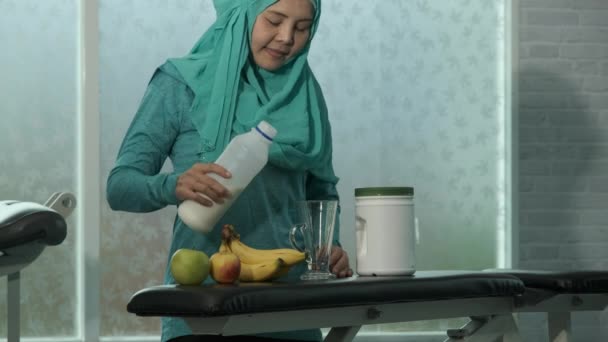 Jonge vrouwelijke moslims in het groen Hijab gieten melk in glas op de bank in de fitnessruimte. sport, bodybuilding, fitness en mensen concept - Video
