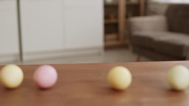 Primo piano di uova sfocate colorate sedute sul tavolo, giocosa ragazza africana sbirciando sotto il tavolo, prendendo un uovo rosa e tornando indietro - Filmati, video
