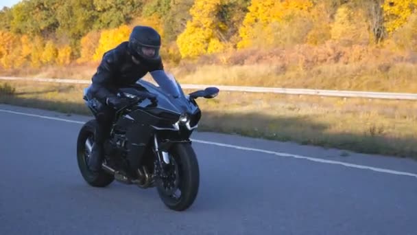 Young man in helmet riding fast on modern sport motorbike at autumnal highway. Motorcyclist racing his motorcycle on country road with headlights on. Guy driving bike during trip. Concept of freedom - Footage, Video