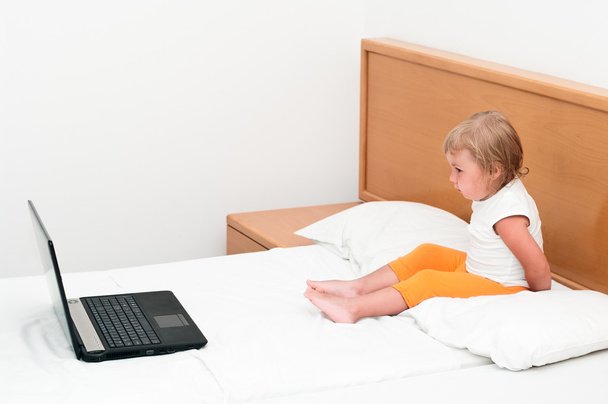 Little child sitting with a laptop on the bed. - Fotografie, Obrázek