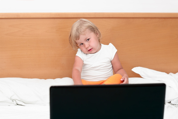 Little child sitting with a laptop on the bed. - Foto, afbeelding