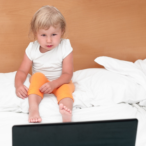 Little child sitting with a laptop on the bed. - Fotó, kép