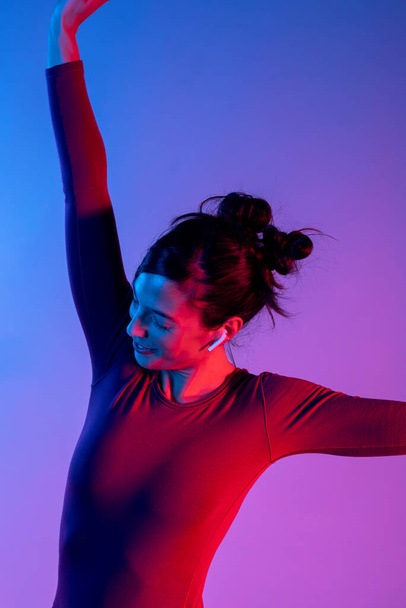 Kulaklıklı çekici bir kadın müzik dinliyor ve stüdyoda mavi ve kırmızı ışıklarla dans ediyor. - Fotoğraf, Görsel