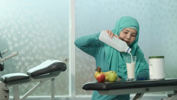 Yeşil tesettürlü genç kadın Müslümanlar spor salonundaki bankta duran bardağa süt döküyorlar. spor, vücut geliştirme, spor ve insan konsepti - Video, Çekim