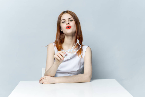 fröhliche elegante Frau mit roten Lippen sitzt am Tisch Brille in Händen Studio - Foto, Bild