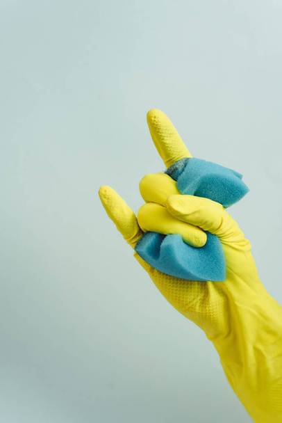 gele rubberen handschoen houdt spons vast op de witte achtergrond. Geel rubber handschoen toont steen teken - Foto, afbeelding
