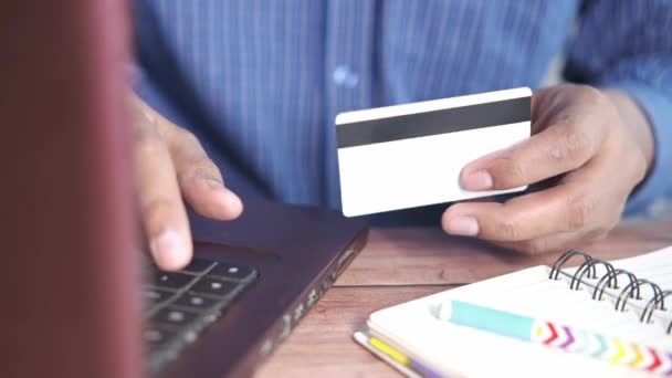 мужчина держит в руках кредитную карту и совершает покупки онлайн с помощью ноутбука  - Кадры, видео