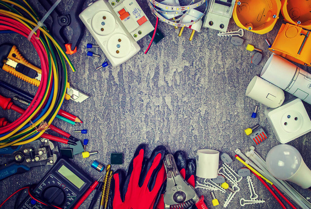 Elektrisch gereedschap en een set componenten voor gebruik in elektrische installaties op een grijze achtergrond met plaats voor tekst - Foto, afbeelding