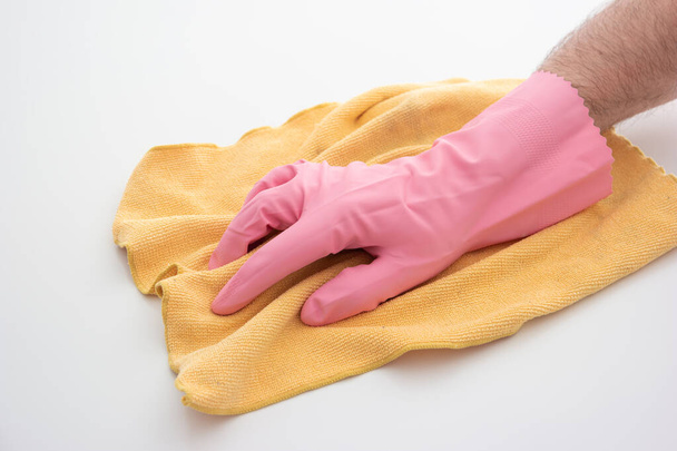 Ροζ γάντι καθαρισμού λάτεξ σε λευκό ανδρικό χέρι κρατώντας ένα κίτρινο πανί μικροϊνών κάνοντας χειρονομία καθαρισμού απομονωμένη σε λευκό φόντο. - Φωτογραφία, εικόνα