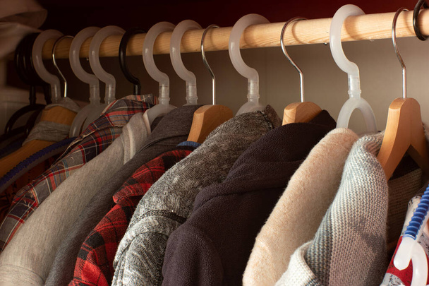 Ряд различных разноцветных предметов одежды на вешалках внутри домашнего шкафа красный деревянный шкаф. - Фото, изображение
