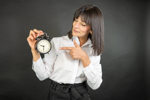 Businesswoman standing on black background and holding vintage alarm clock  - Foto, imagen