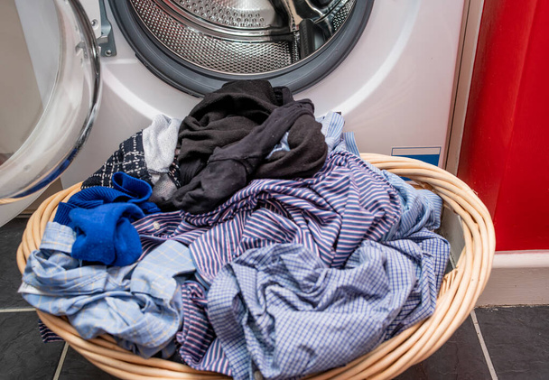 7 Ein unscharfer Weidenkorb voller nasser Wäsche vor einer Waschmaschine in scharfem Fokus - Foto, Bild