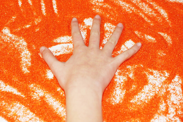 Sandtherapie, Hand des Kindes auf orangefarbenem Sand. - Foto, Bild
