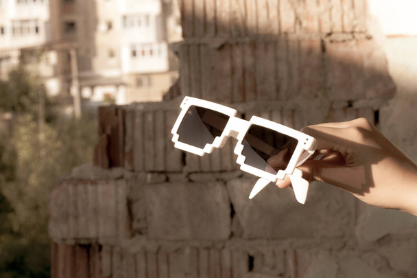 Білі піксельні сонцезахисні окуляри з чорними лінзами тримаються в руці крупним планом в сонячний день. Вибірковий фокус
 - Фото, зображення