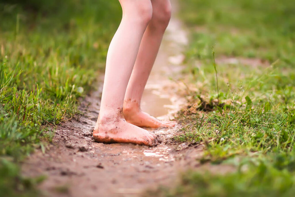 Chica descalza camina a través de un charco de agua después de la lluvia de verano en el campo. - Foto, Imagen