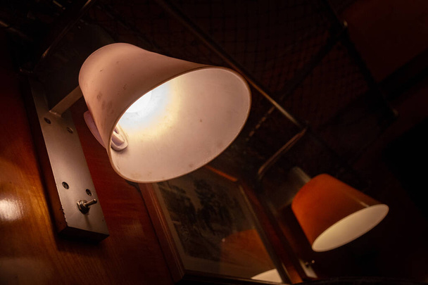 Dwie lampy z białymi abażurami wiszące na drewnianej ścianie w ciemnym pokoju - Zdjęcie, obraz