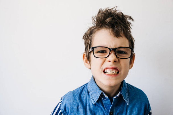 Portret chłopca z autyzmem w okularach w niebieskiej koszuli na białym tle grymasów. Świadomość autyzmu i pojęcie bólu - Zdjęcie, obraz