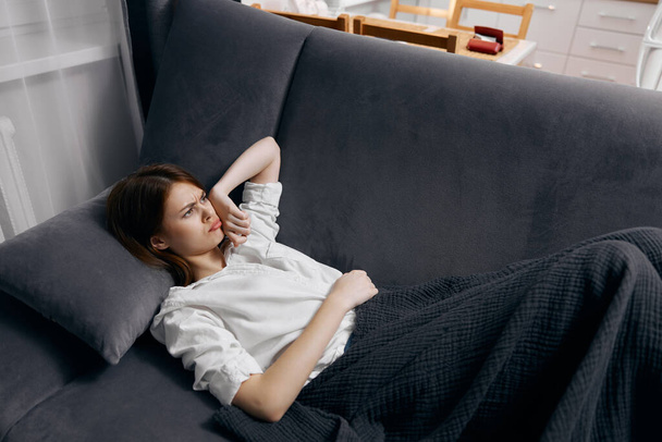 Женщина в белой футболке лежит на диване под одеялом - Фото, изображение