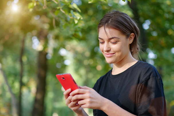 Beautiful young woman looks in his smartphone and smiles - Photo, Image