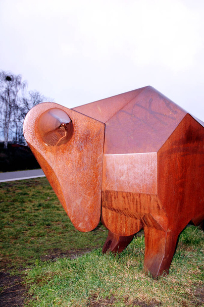 Скульптура быка ржавый металл на траве перед небом с тонкими граффити - Фото, изображение