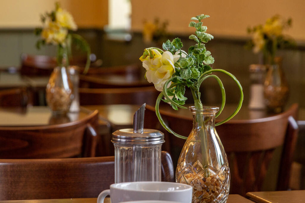 Flores amarillas en un jarrón de vidrio junto a un tarro de azúcar en una mesa de café - Foto, Imagen